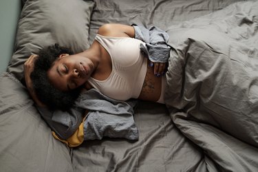 Young tired female sleeping under grey blanket